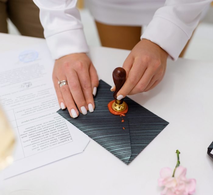 Close up of anonymous woman, bride with rights on fingers hand putting red stamp on grey envelope during engaged ceremony